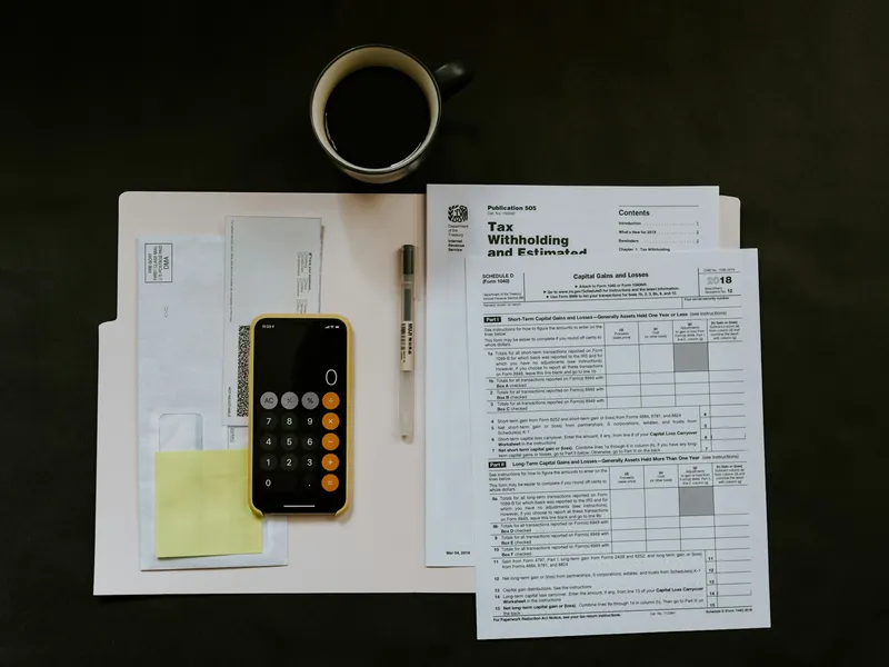 Tax paperwork, a pen and a phone on a white folder on a desk
