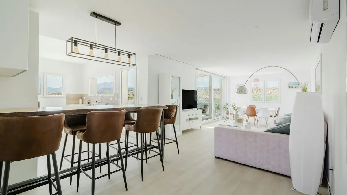 Salón y cocina abierta luminosos, con muebles despejados y luz natural entrando por un ventanal