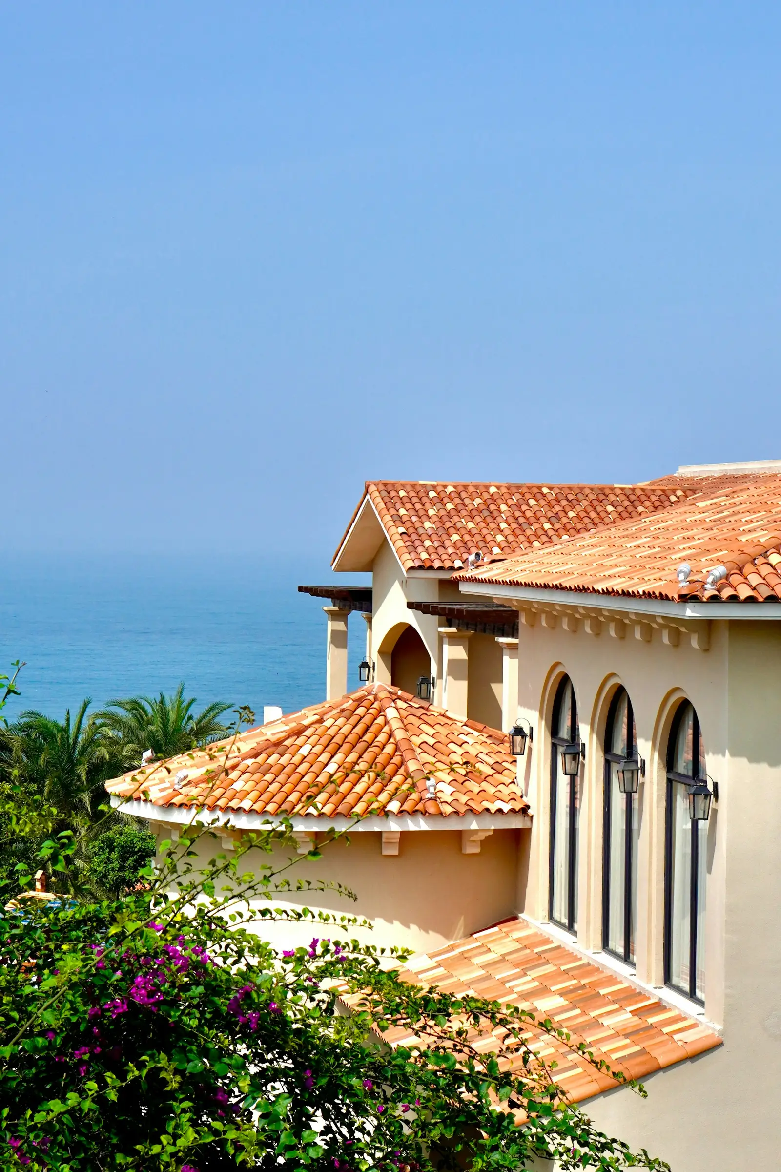 Villa mediterránea con tejado de teja y vistas al mar, buganvilla en primer plano